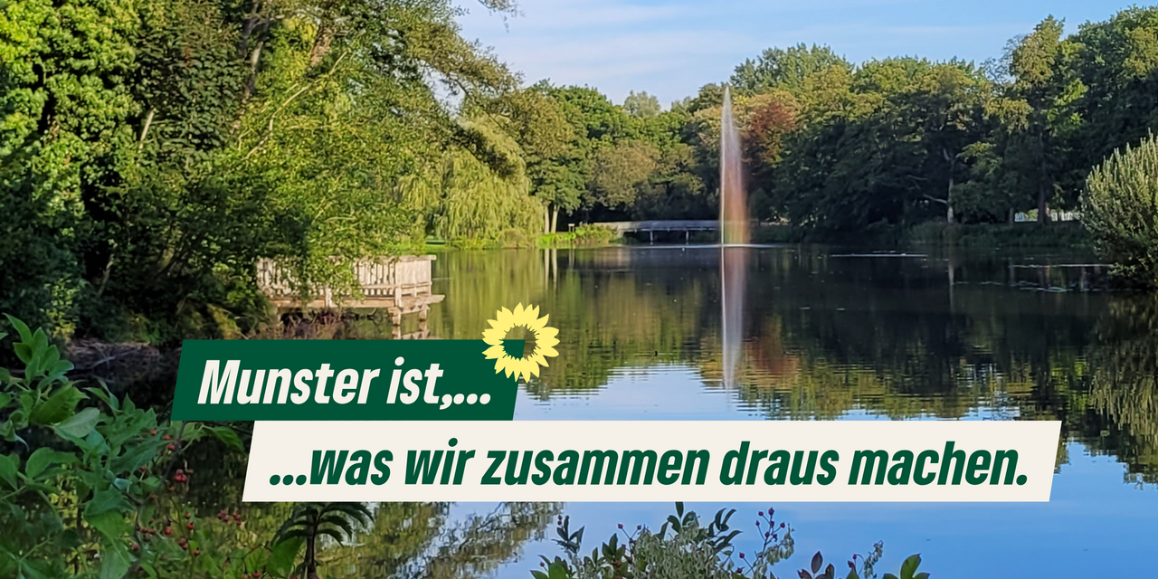 Der Mühlenteich in Munster, blauer Himmel, grüne Bäume, eine Wasserfontäne mit Regenbogen